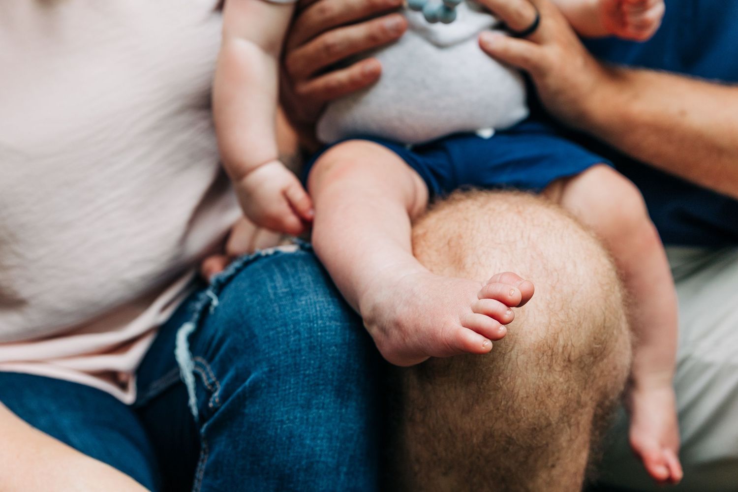 A family sits together on their front porch steps sharing a tender moment with their baby wearing a teal pacifier.