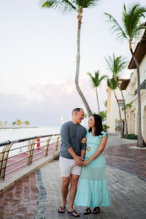 A romantic couple shares tender moments along a palm-lined beachfront walkway at sunset.
