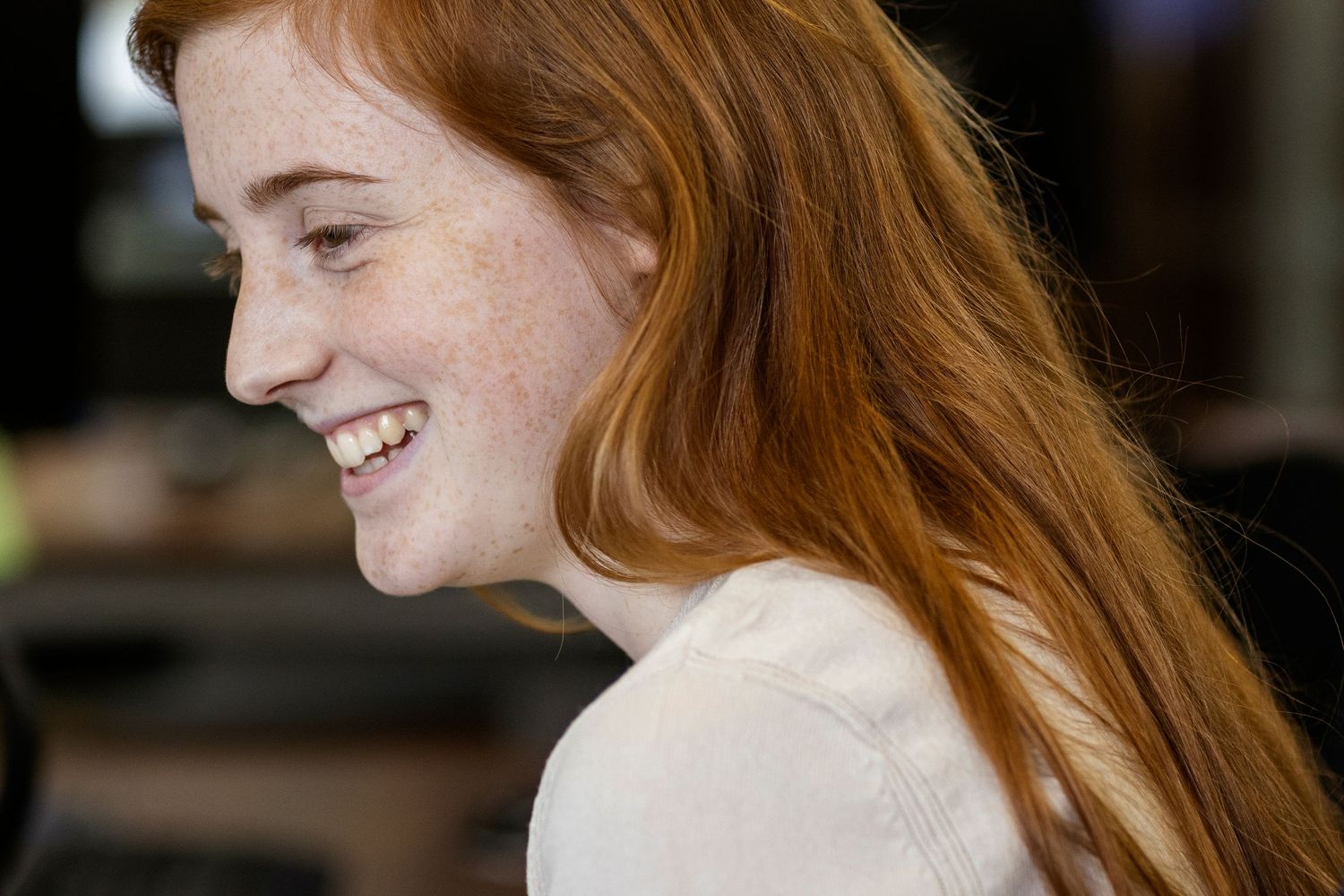 Profile view of someone with long red hair and freckles smiling brightly in a candid moment.