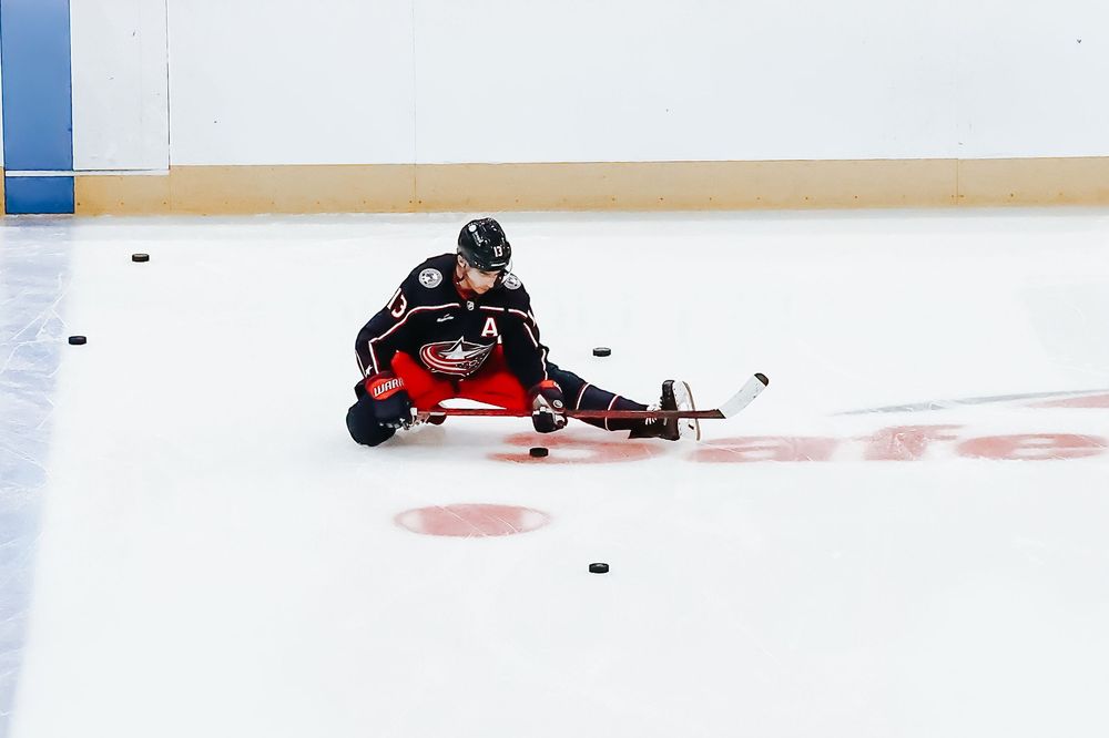 Hockey player slides across ice rink while reaching for loose puck during intense gameplay action.
