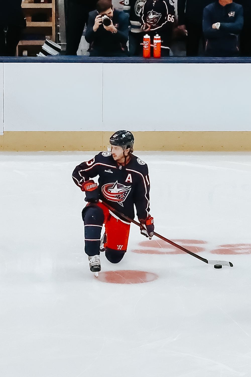 Hockey player in Columbus Blue Jackets uniform slides across ice during NHL game action.