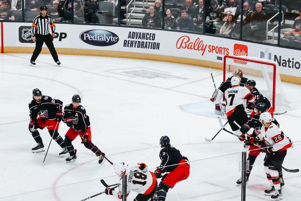 Hockey players compete for the puck during an intense game on the ice rink with sponsors visible on the boards.