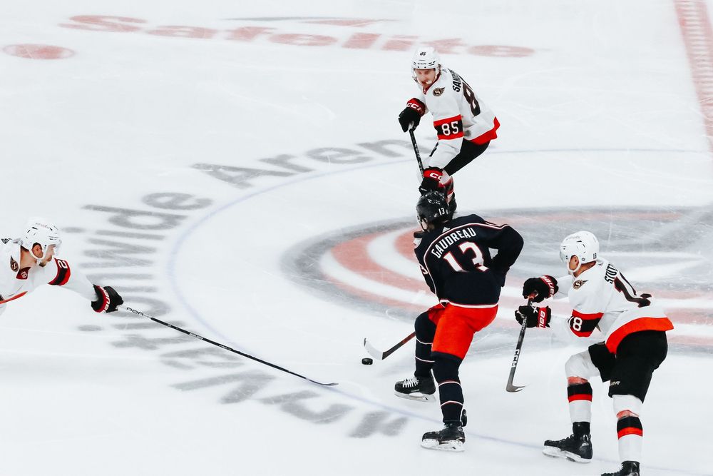 Ice hockey players in black and red uniforms battle for control of the puck during an intense game.