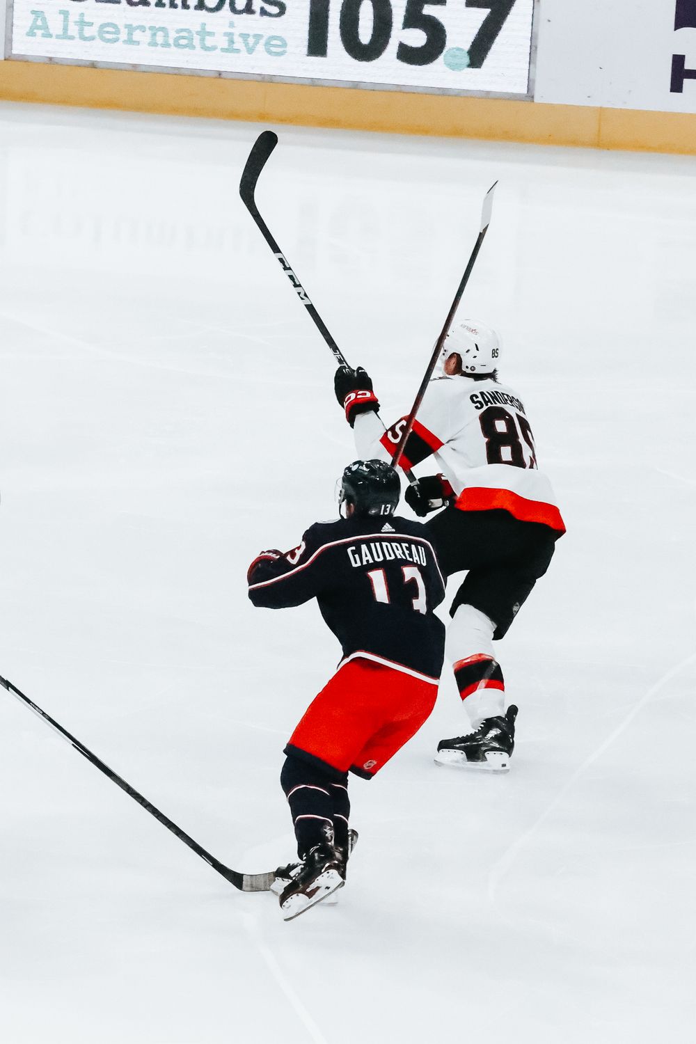 Hockey player in black and red jersey performing an acrobatic flip move on the ice during a game.