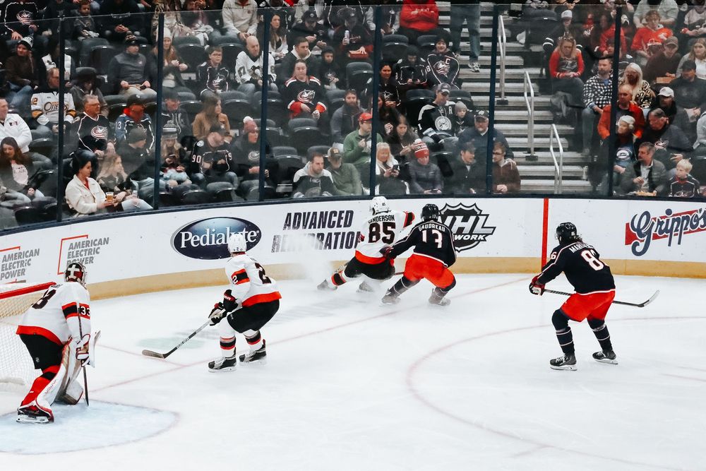 Hockey players compete for the puck during a professional ice hockey game with spectators in the background.