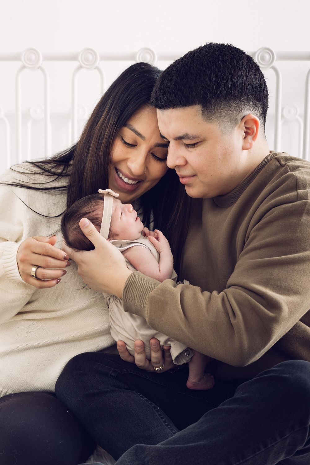 Smiling young parents sitting together tenderly holding their newborn baby indoors.