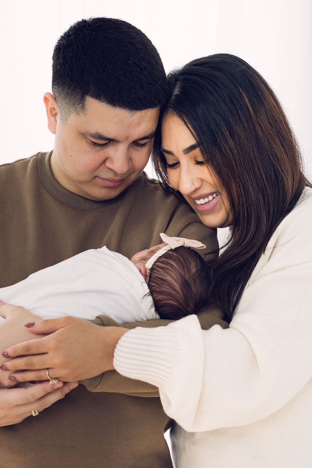Young couple standing close together lovingly cradling their swaddled newborn baby.