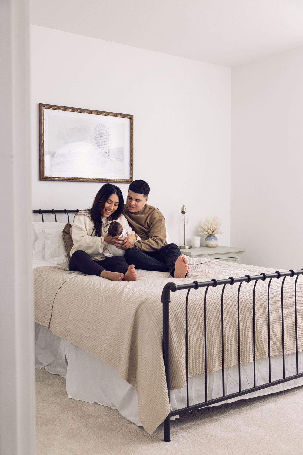 Young couple sitting on bed admiring their newborn baby in a bright modern bedroom.