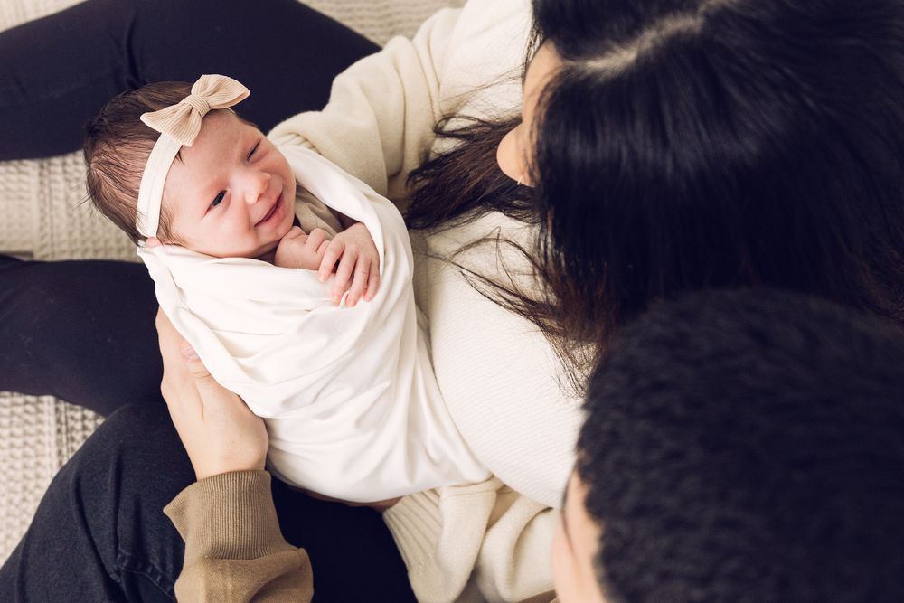 Mother gazing lovingly at her swaddled newborn baby girl wearing a bow headband.