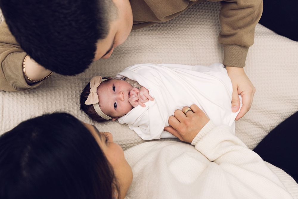New parents looking down at their swaddled newborn baby girl with a bow headband.