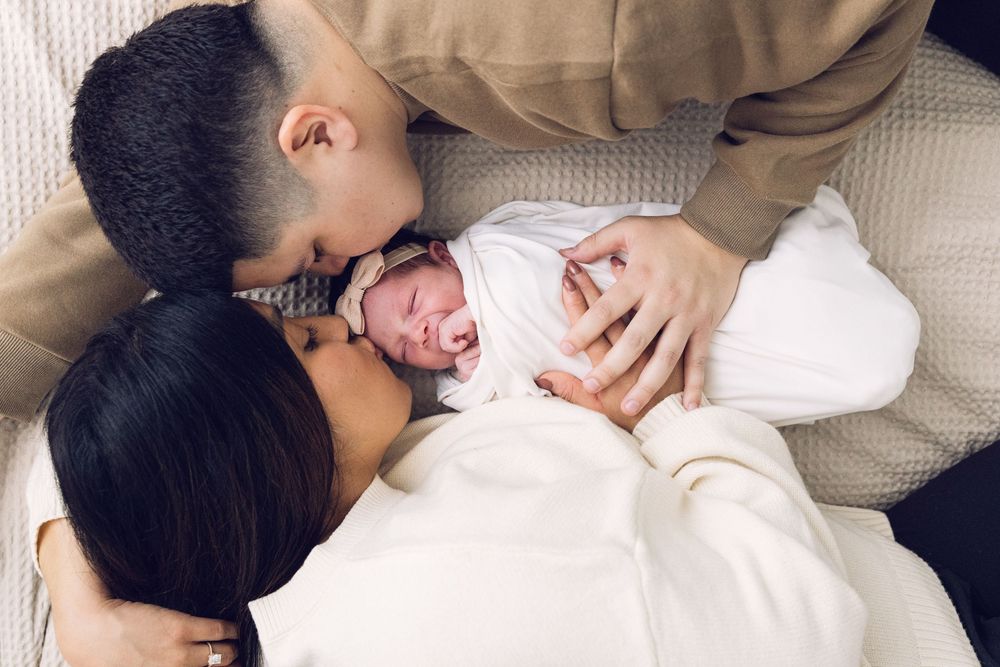 New parents kissing their crying newborn baby together in a tender moment.