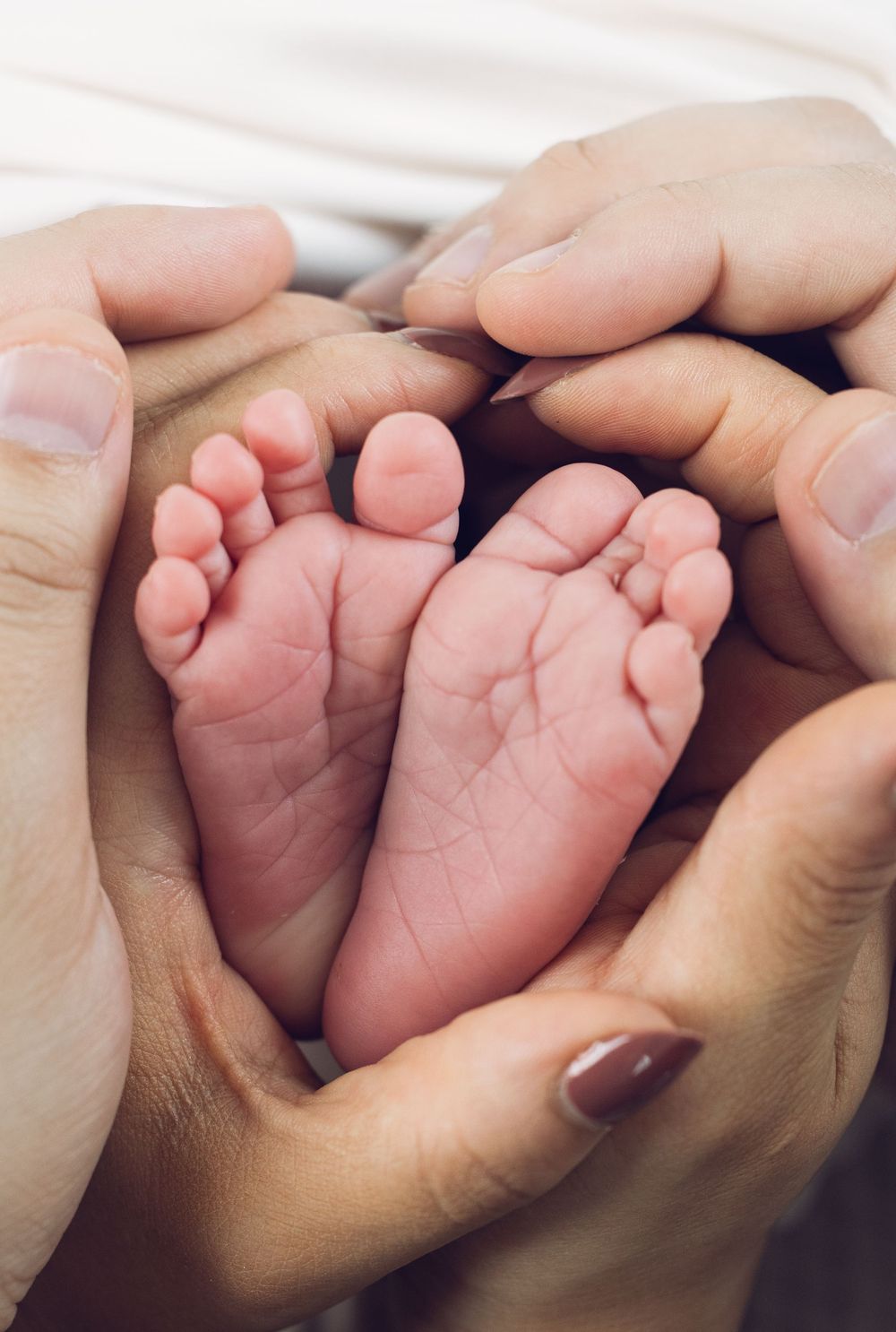 Parents cradling tiny newborn baby feet in their hands in a heart shape.