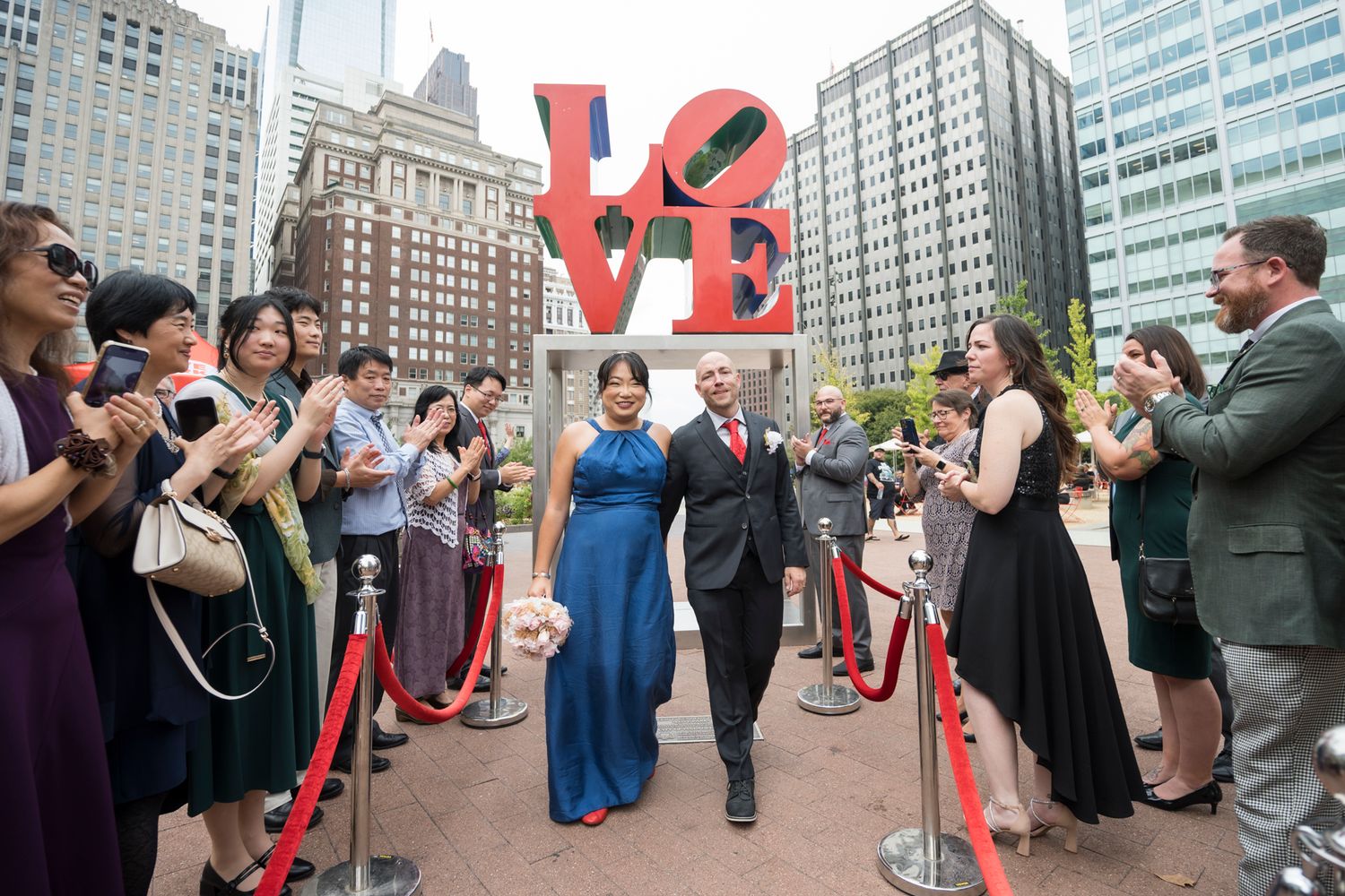 Tourists and visitors gather around the iconic LOVE sculpture in Philadelphia's Love Park on a sunny day.