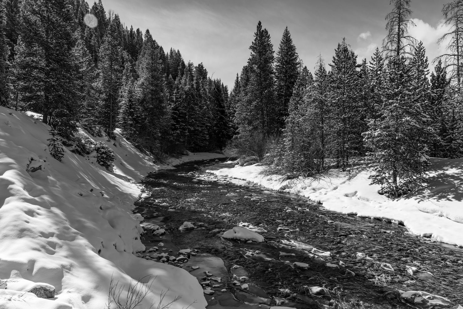 Long exposure black and white winter river landscape photography showing winding river thru snowy mountain forests, calming nature wall art.