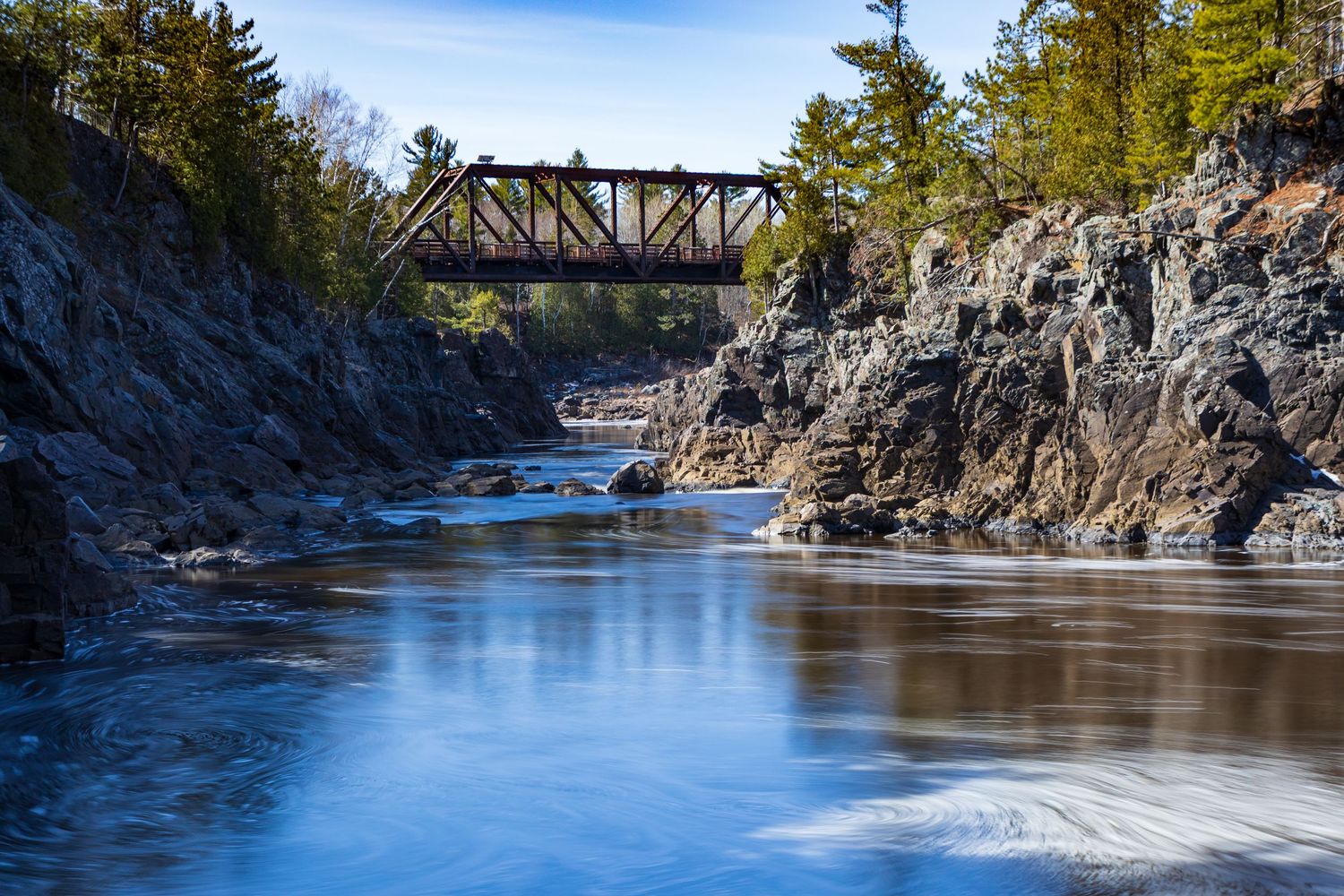 Long exposure waterfall landscape photography showing cascading water between rocky cliffs with railroad bridge, calming nature wall art.