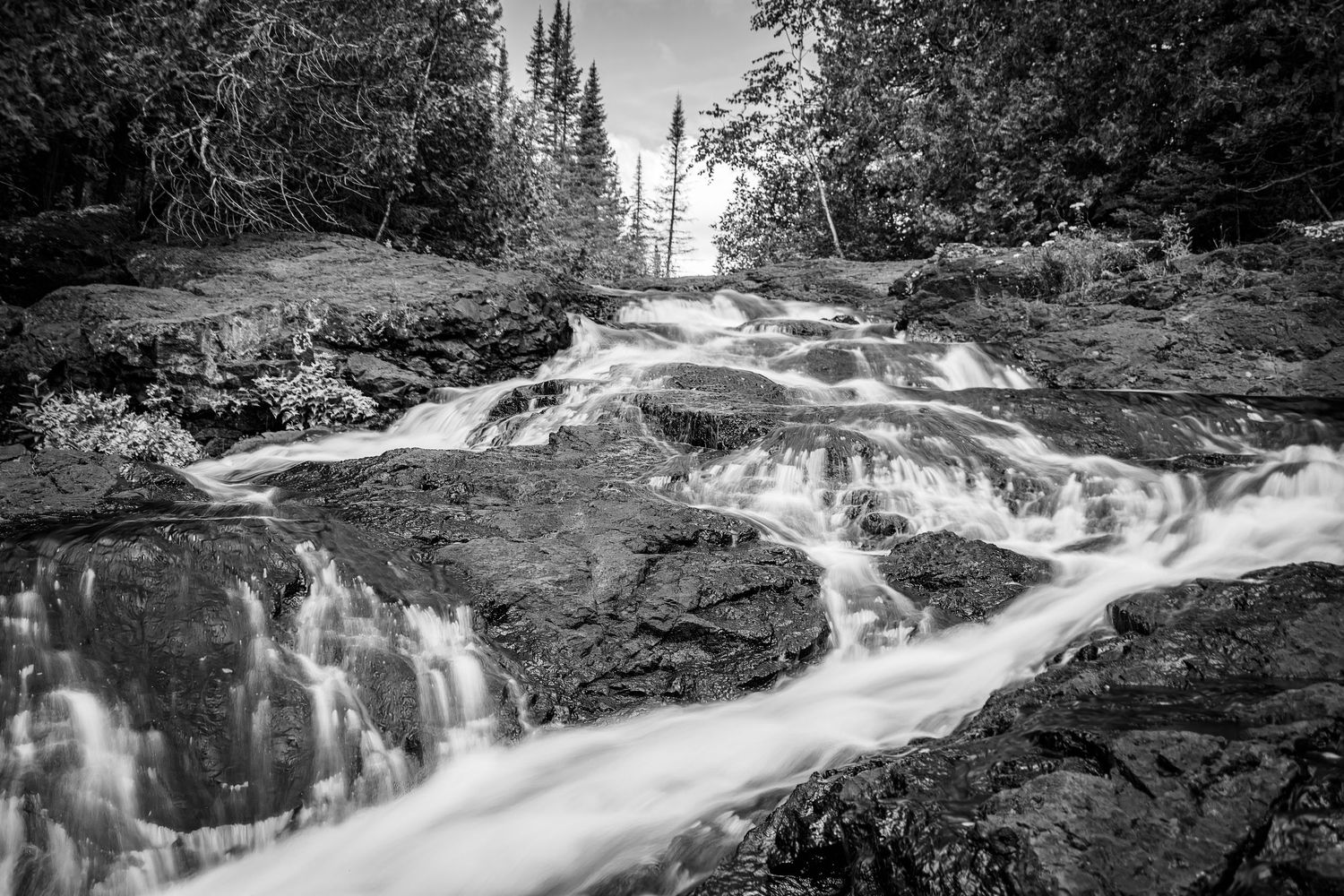 Long exposure black and white waterfall landscape photography showing cascading water over mossy rocks in forest, calming nature wall art.