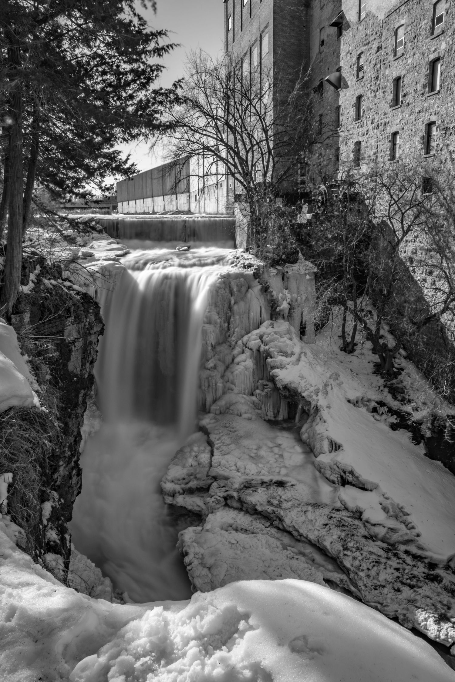 Long exposure black and white winter waterfall landscape photography showing cascading water over icy in Minnesota, calming nature wall art.