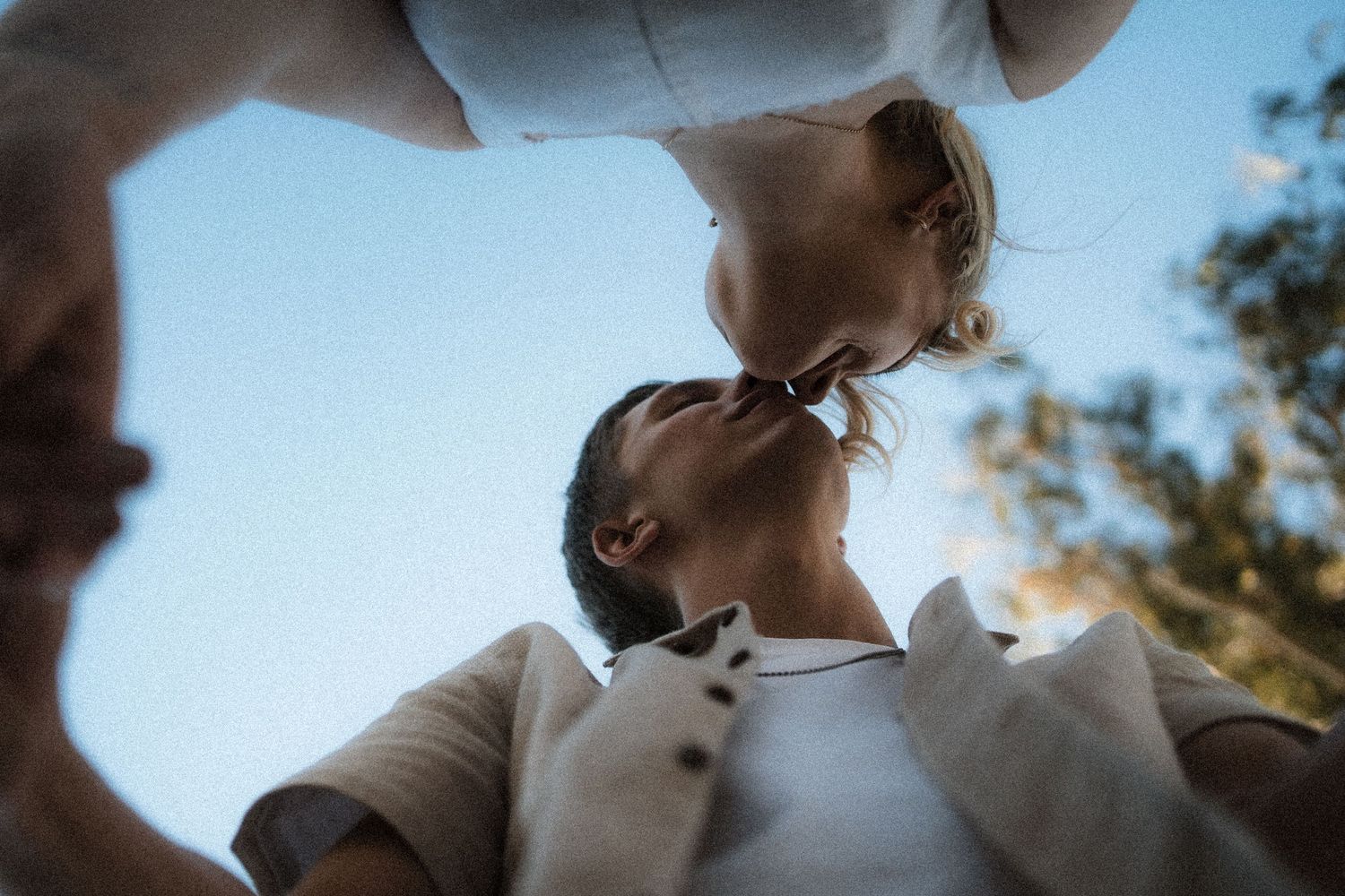 A romantic couple shares an intimate moment outdoors on a sunny day, captured from a low angle perspective in Buxton, Victoria by the river