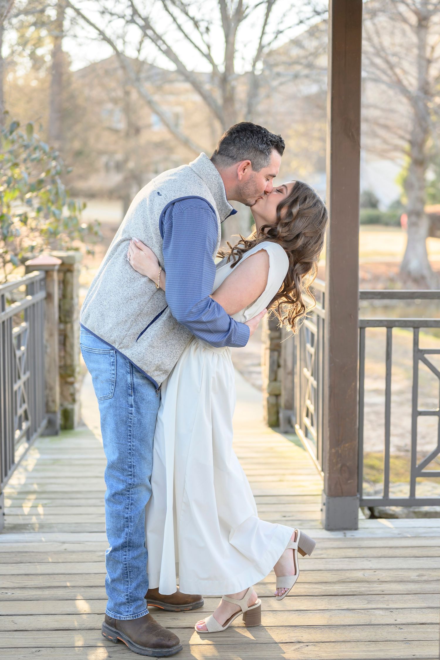 A romantic couple shares a tender kiss on a wooden boardwalk during sunset.