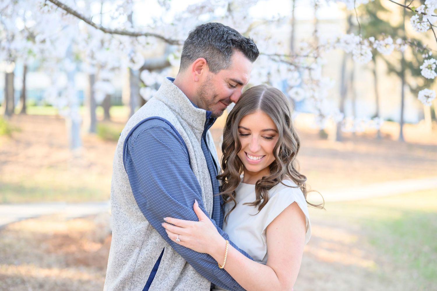 A couple in formal attire embraces romantically in an outdoor setting with golden sunlight filtering through trees.
