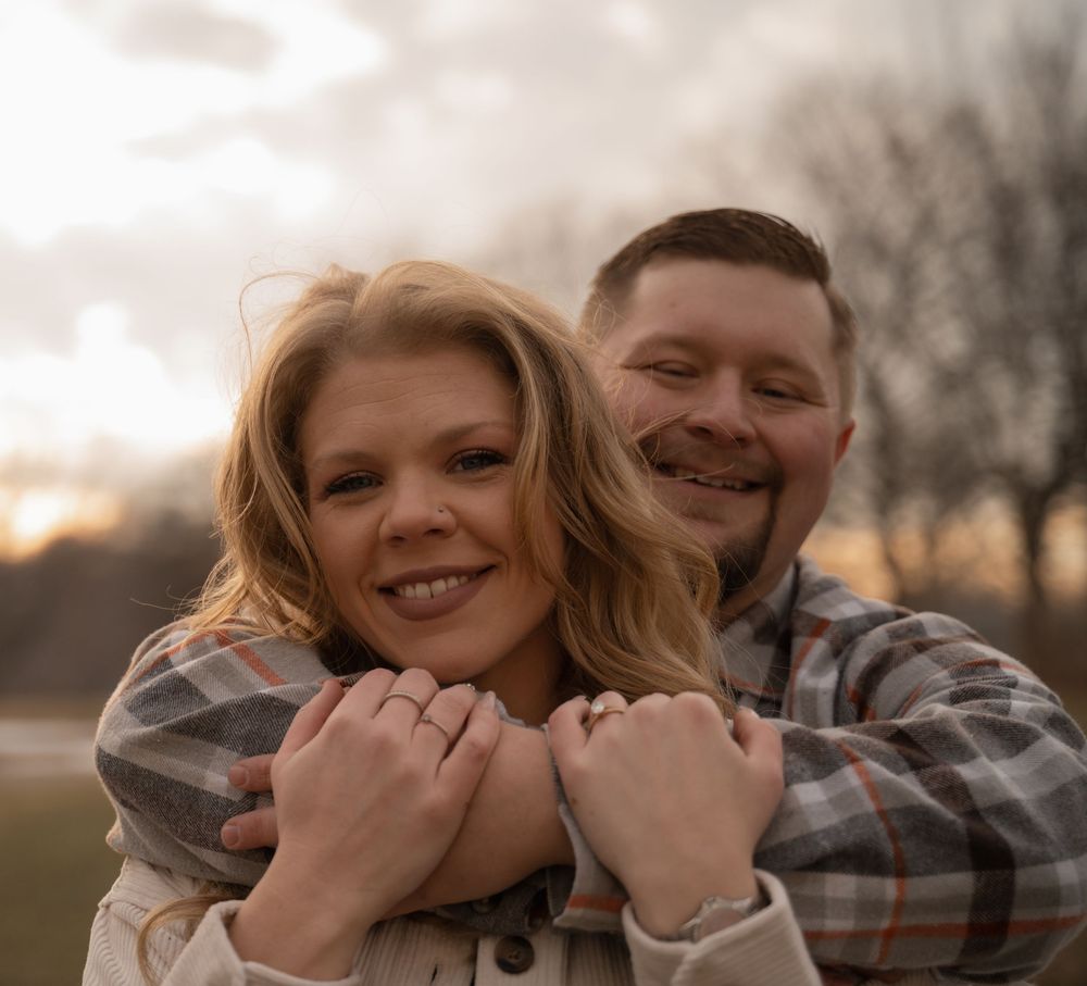 A couple embraces outdoors during a romantic winter photoshoot with bare trees in the background.
