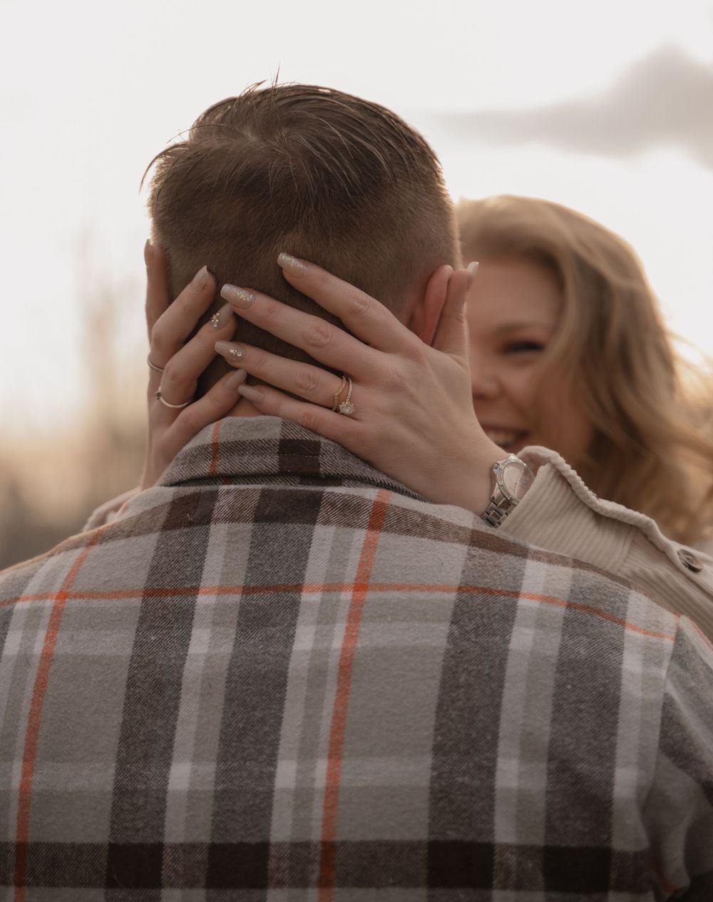 Intimate embrace between couple in plaid shirt during sunset outdoors.