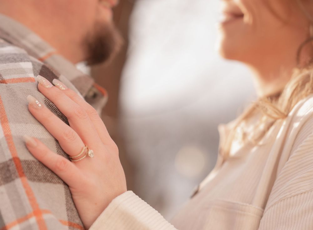 Close-up shot of hands wearing engagement ring and wedding band against a light neutral background.