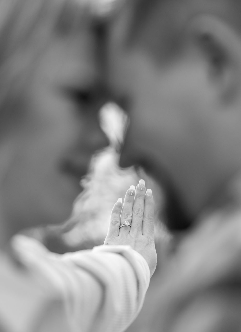 A raised hand with a ring shown in soft black and white focus against a blurred background.