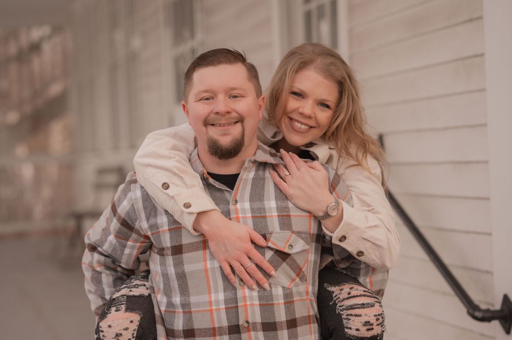 A couple shares joyful moments together outdoors against a light-colored wall background.