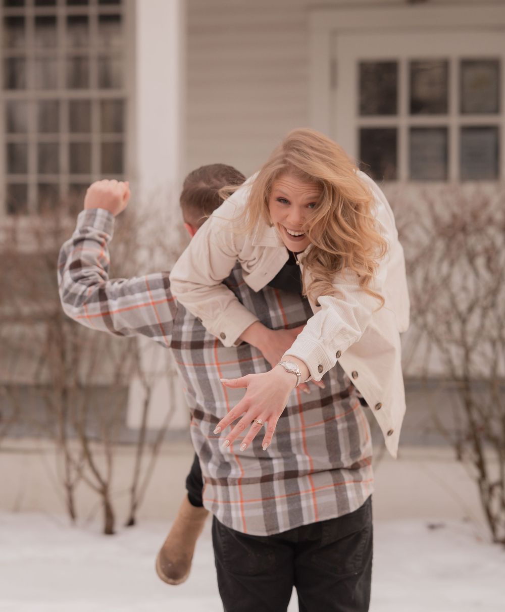 A couple dances together in the snow, with the woman wearing a light colored coat and the man in plaid.