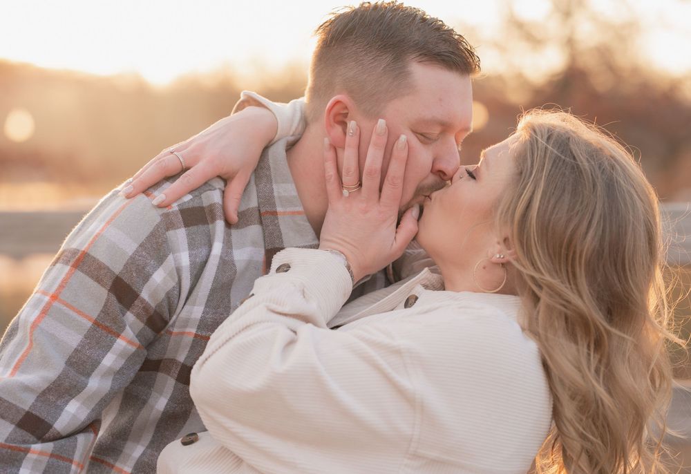A romantic couple shares a tender kiss at sunset while wearing casual attire in a warm golden light.