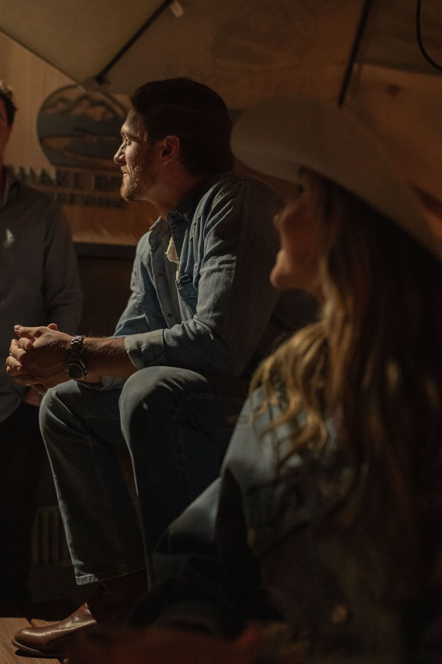 Dimly lit gathering scene with people seated in casual conversation.