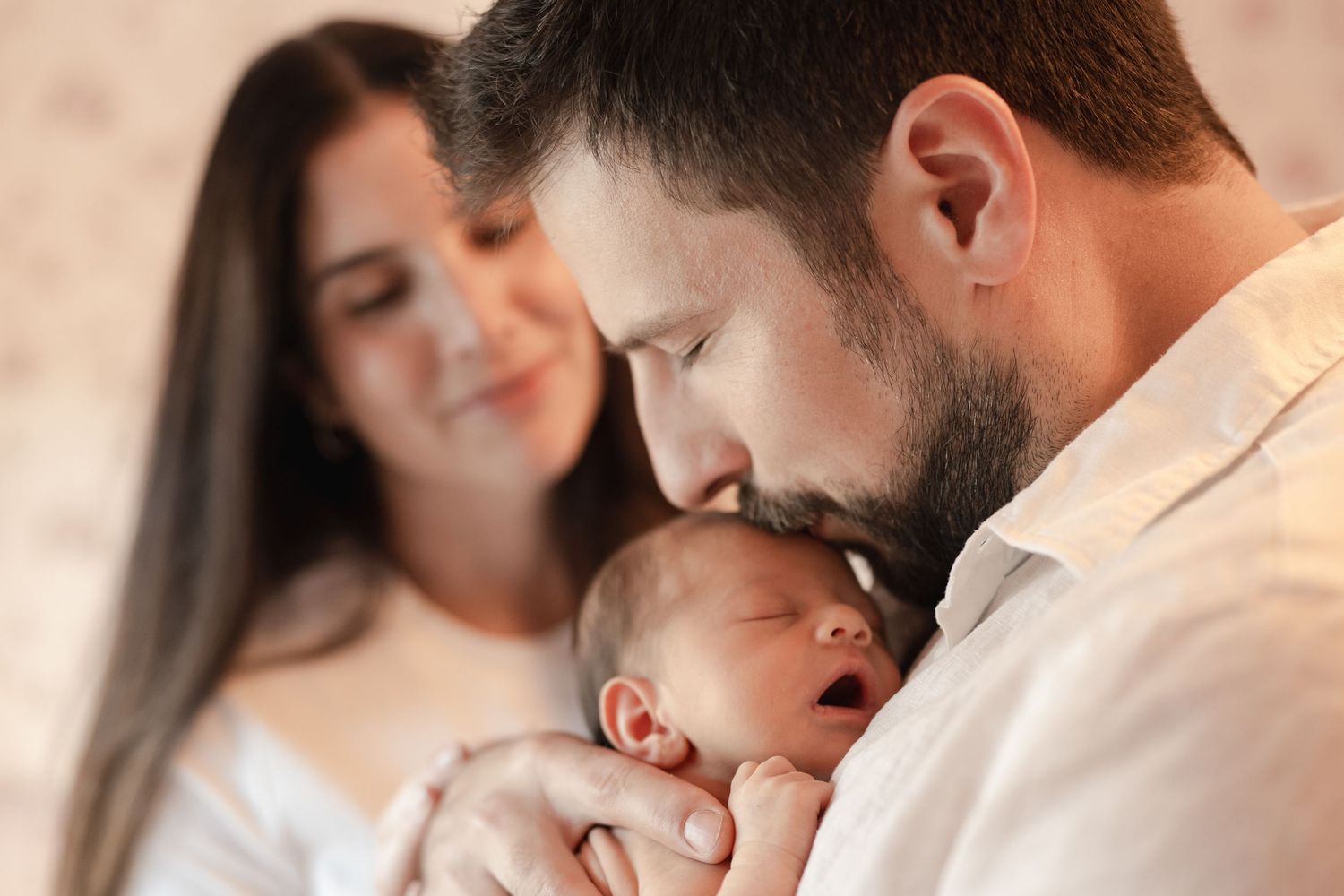 A tender moment as parents bond with their newborn baby in a soft, intimate indoor setting.