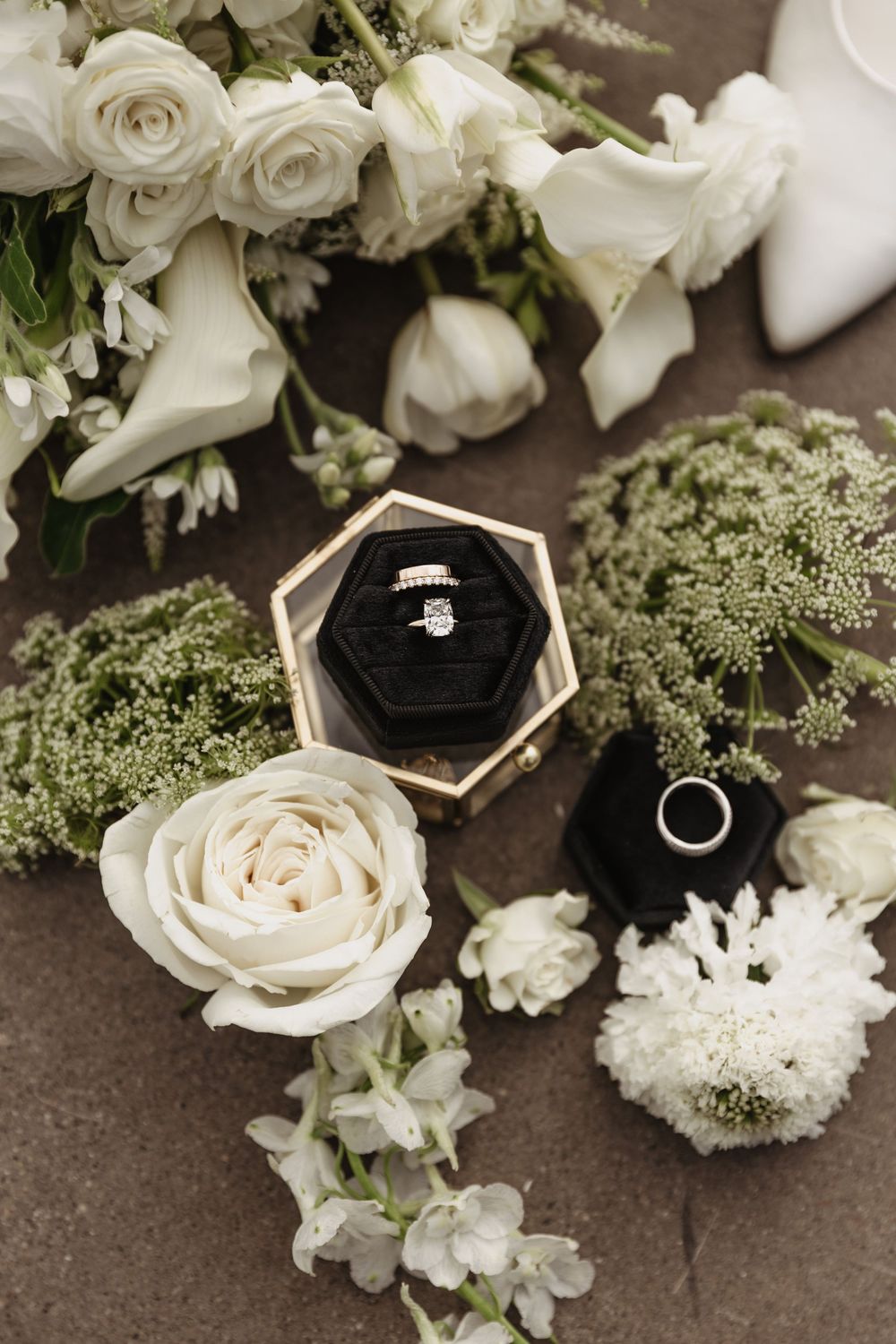 Wedding rings displayed in geometric black and gold boxes among white roses and delicate floral arrangements.