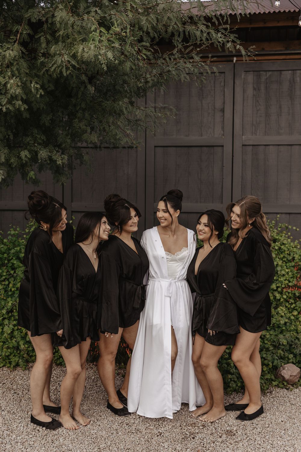 A group wearing black and white outfits pose together in a backyard setting against a wooden fence.