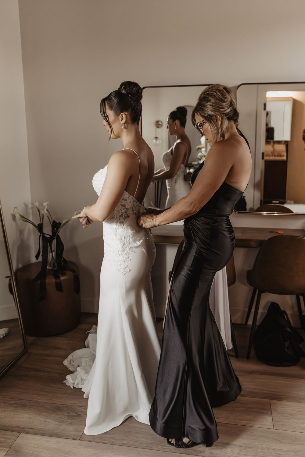 A sequence of images showing someone in a white wedding dress being helped into their gown by an attendant in black.