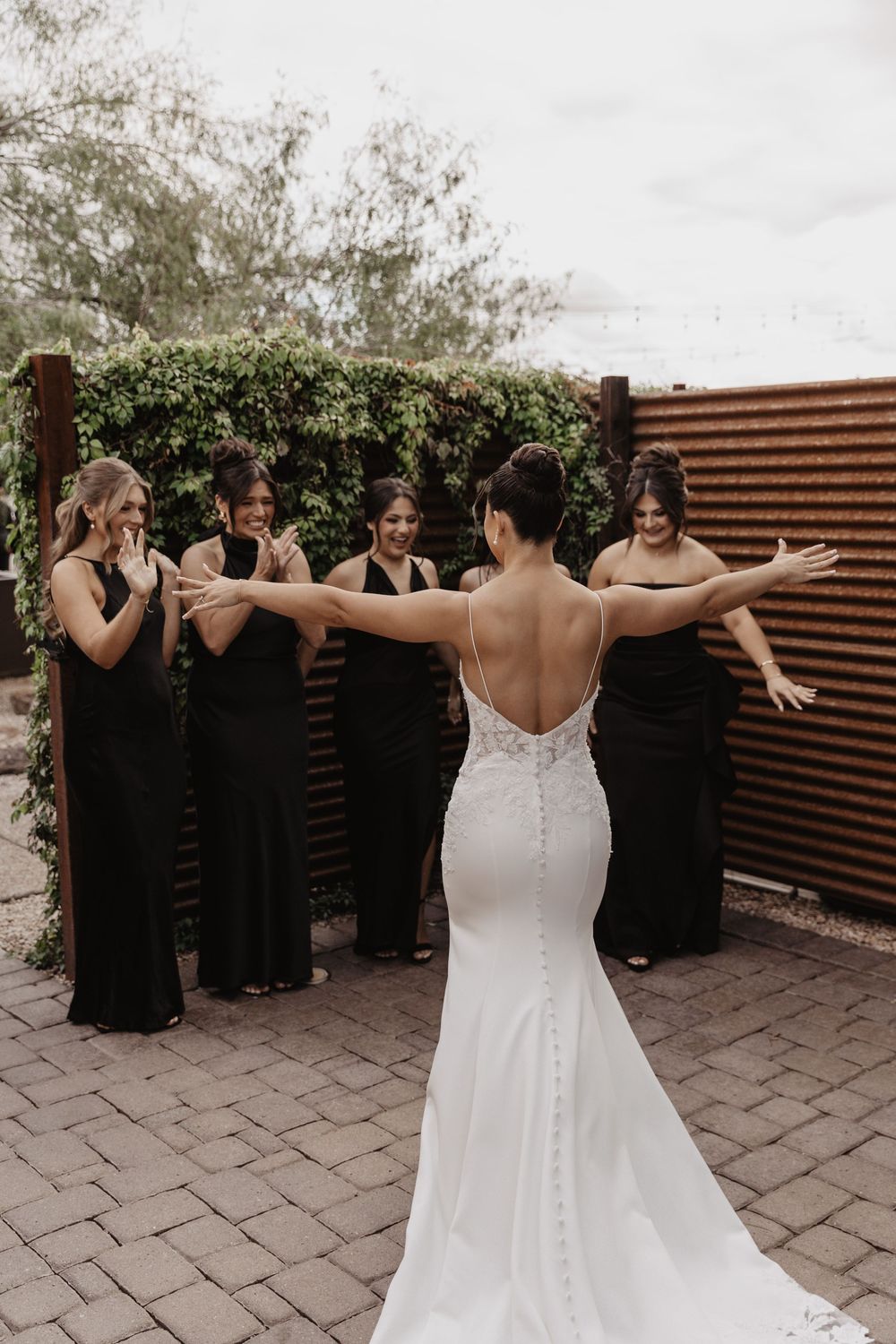 A bride in a white wedding dress shares joyful moments with bridesmaids in black dresses on a patio.