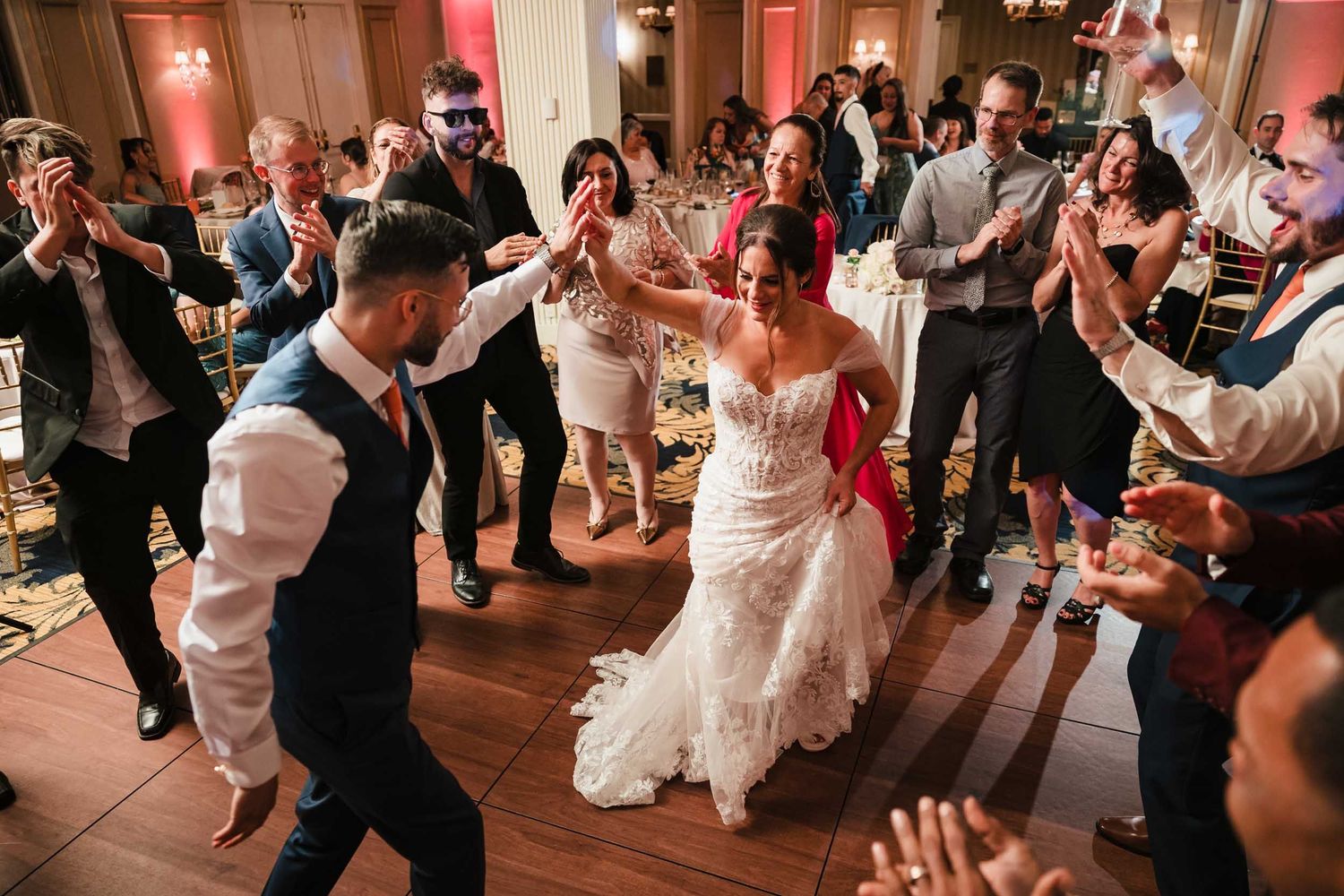 Bride and groom dancing together in the center of a circle of cheering guests during a lively wedding reception at the Lenox Hotel Boston.