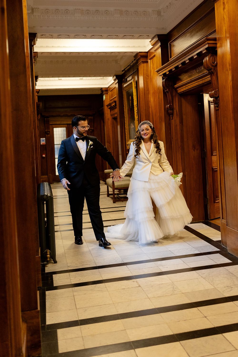 A wedding couple walks through an elegant wood-paneled hallway during their celebration.