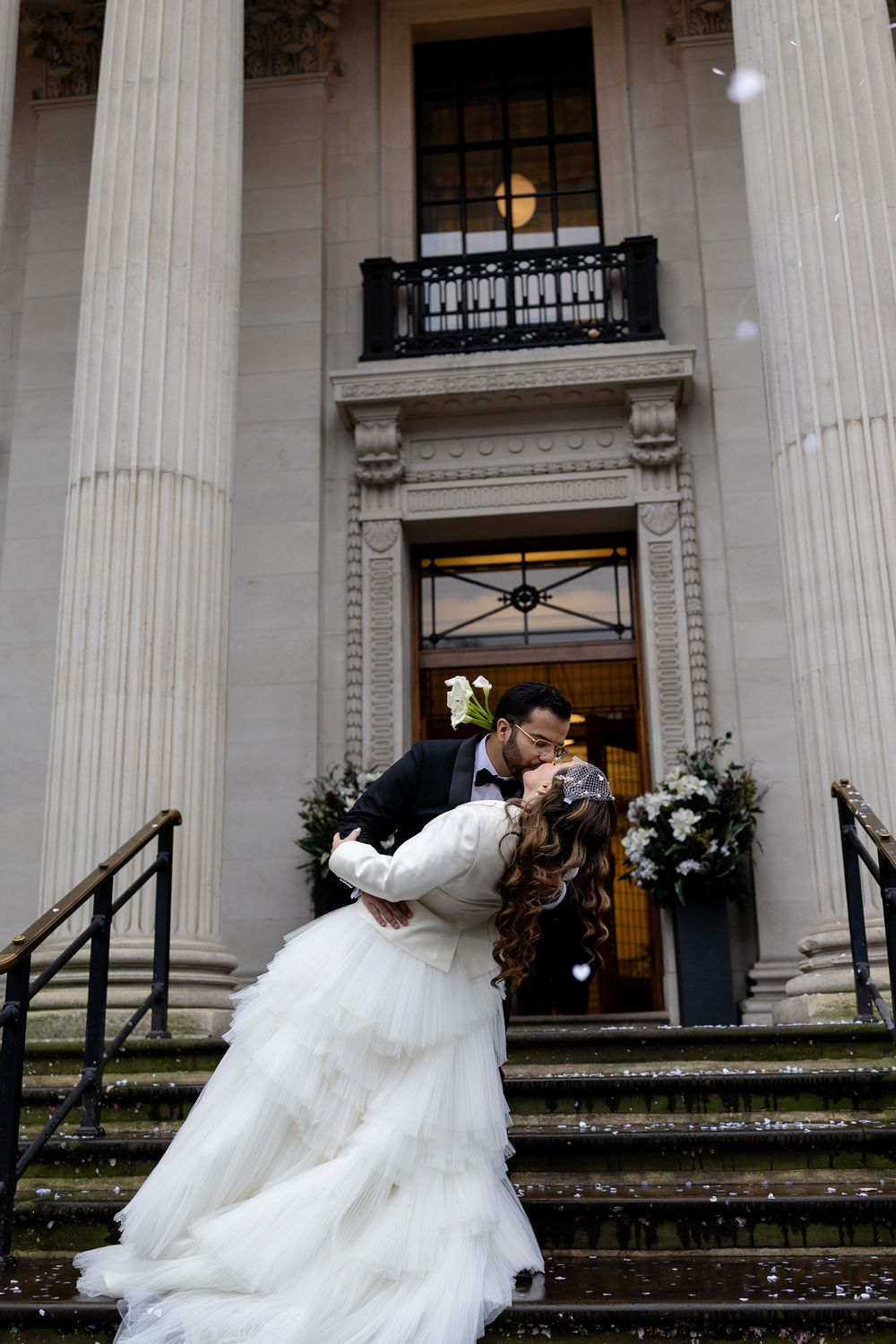 Romantic wedding couple shares dramatic dip kiss on grand stone steps of historic building.
