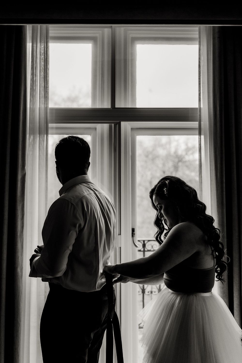 A series of black and white silhouettes by windows show figures in formal attire getting ready for a special occasion.