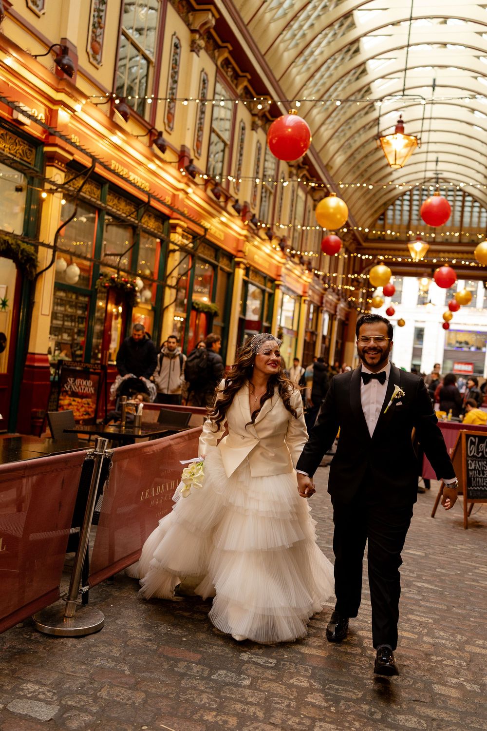 A couple walks through a charming covered market arcade decorated with red lanterns and ornate architecture.