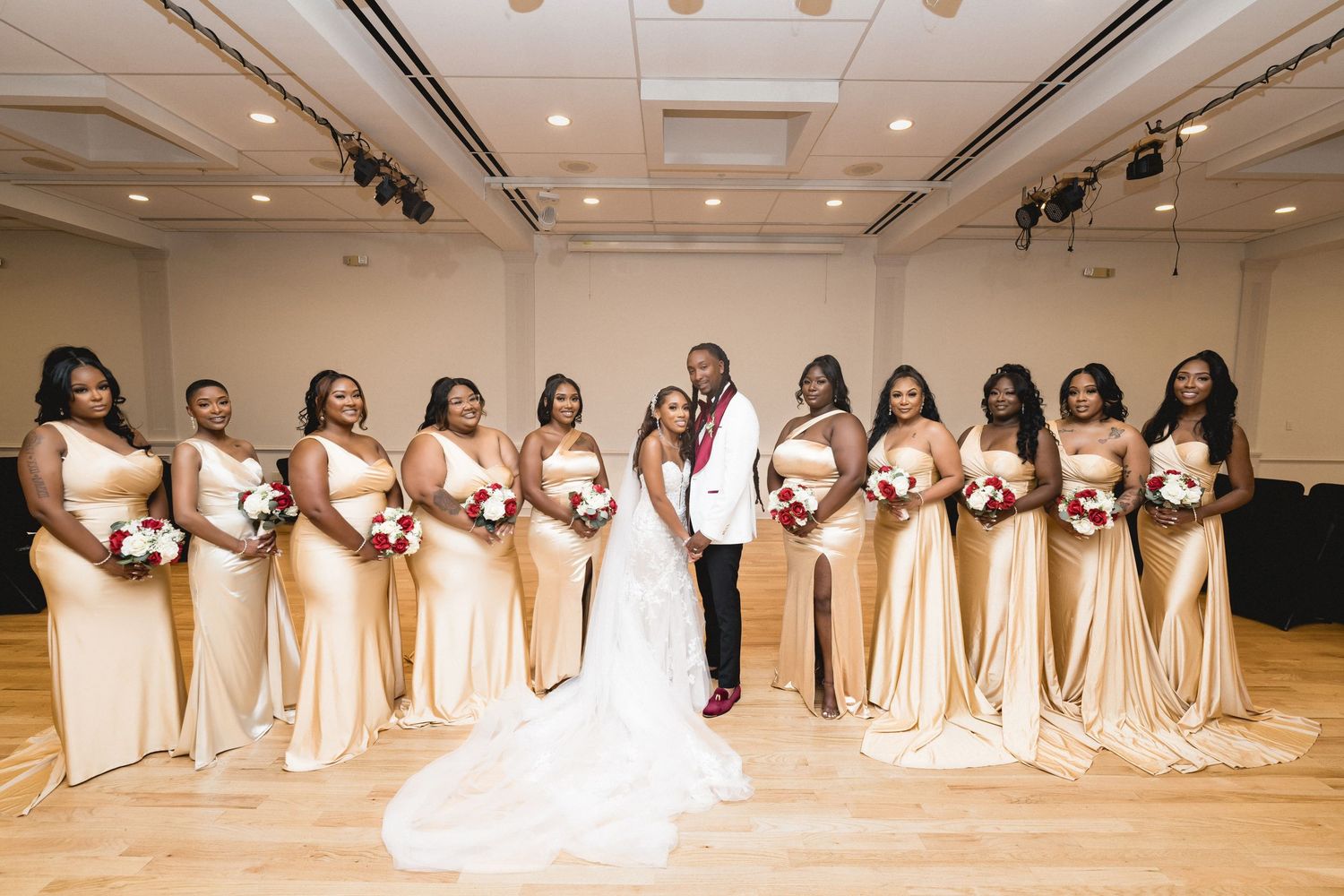 Wedding party in elegant champagne-colored bridesmaid dresses poses with bride in white gown at indoor venue.