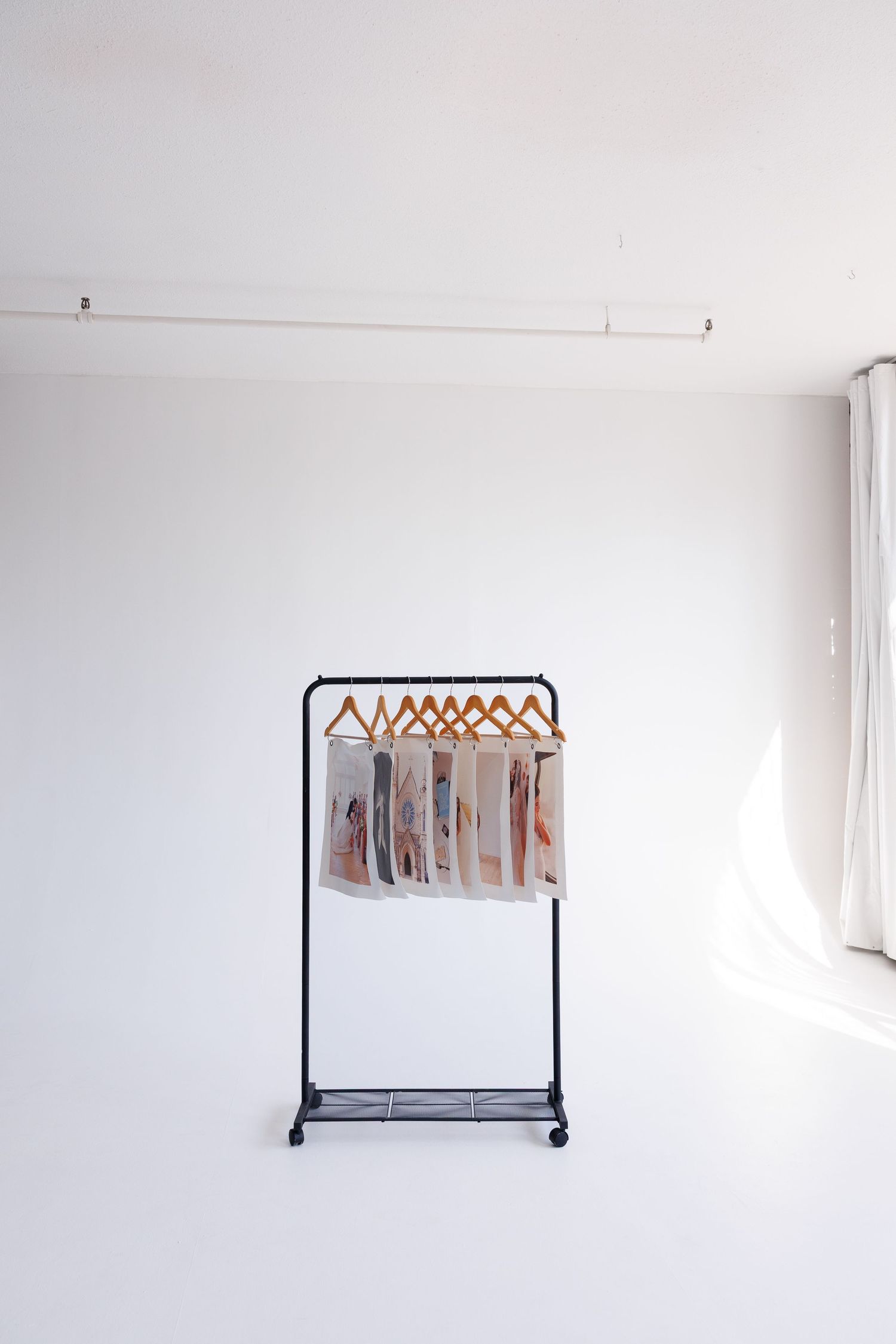 A minimalist clothing rack with wooden hangers stands against a white wall in an empty room.