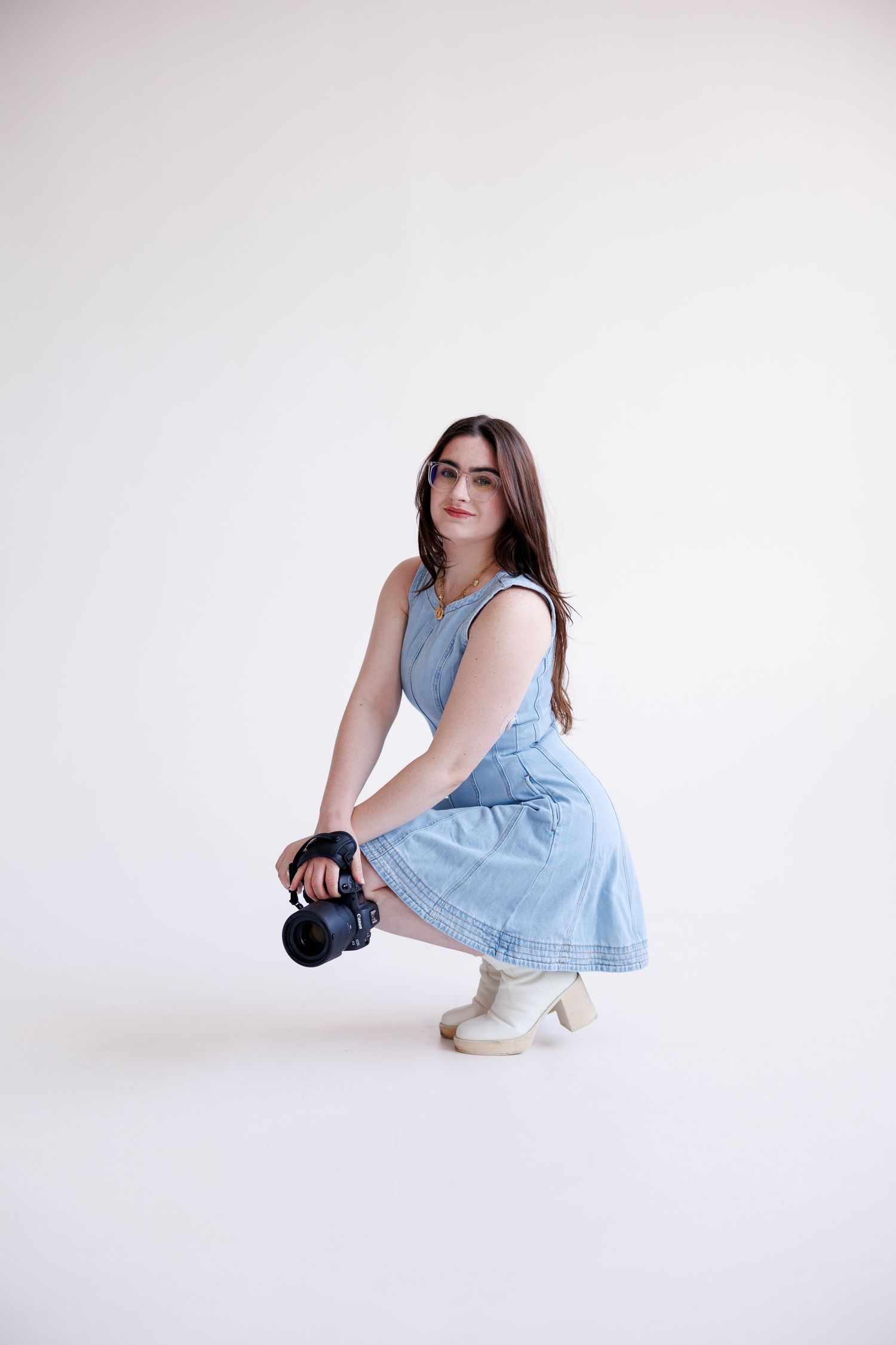 A model in a light blue dress and white shoes poses in various crouching positions against a white studio backdrop.