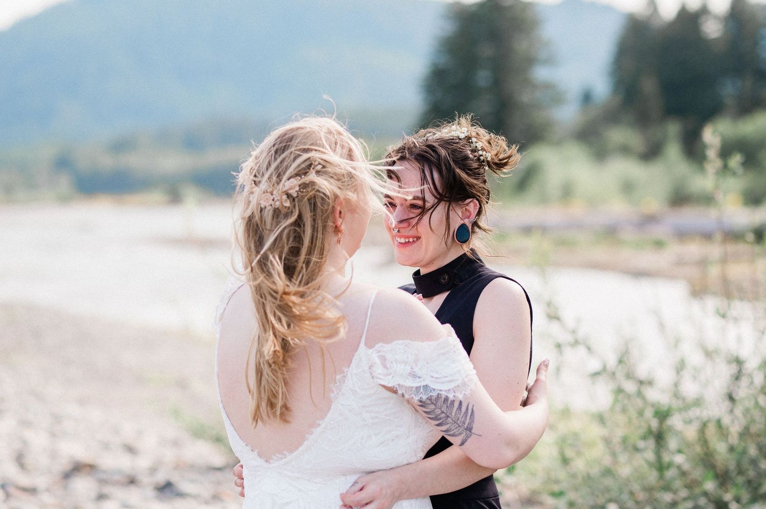 A couple embracing in scenic natural settings with mountains and river behind them on a windy day