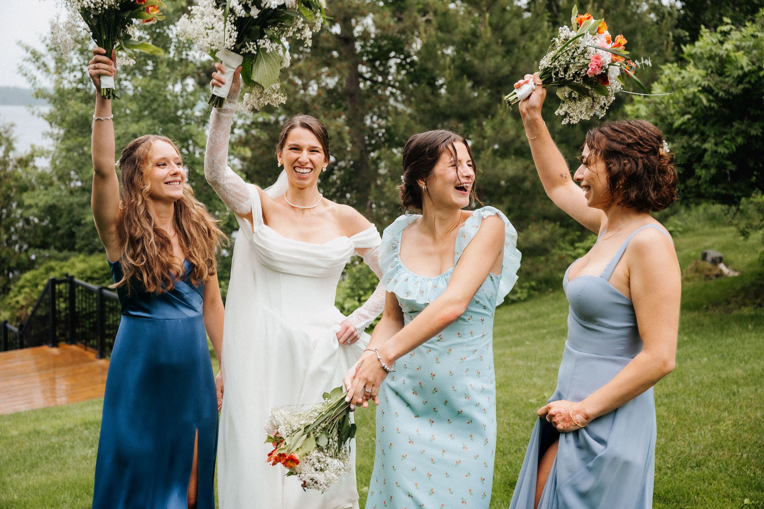 A joyful celebration at an outdoor wedding with bridesmaids in blue dresses holding floral bouquets in a garden setting.