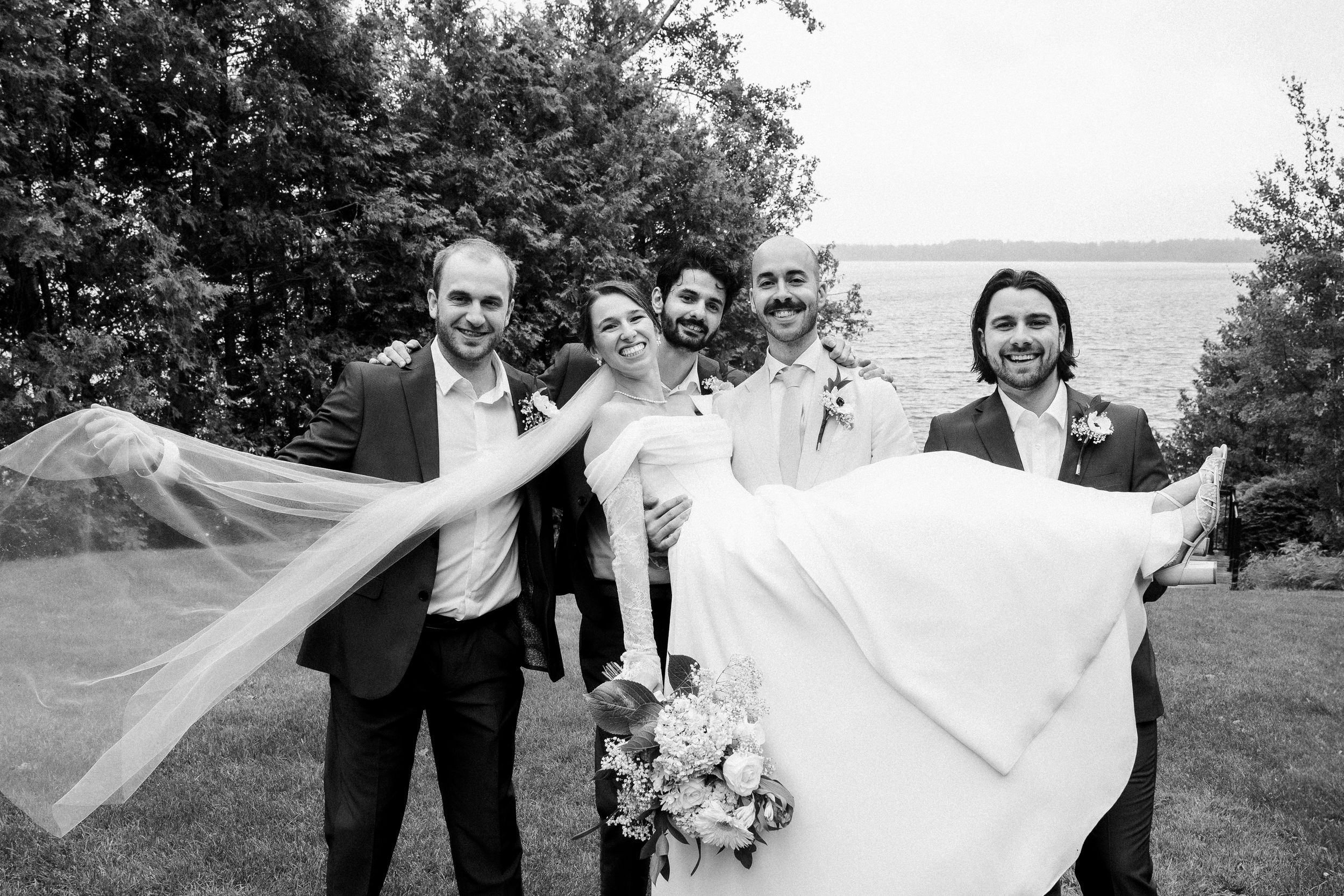 A wedding party lifts a flowing white veil in the air during an outdoor photo session.