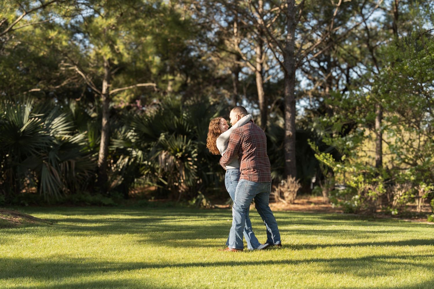 Border collie peeks playfully from behind legs wearing jeans in a sunny outdoor setting.