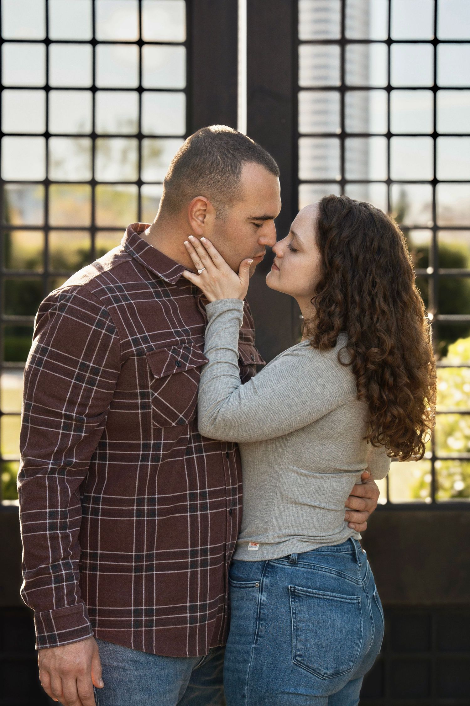 A romantic embrace against a windowed backdrop with natural lighting streaming through.